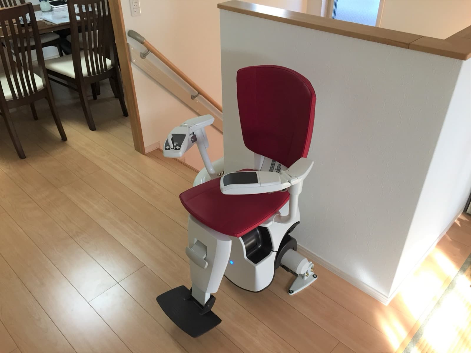 A curved stairlift with a red seat parked at the top landing of a staircase